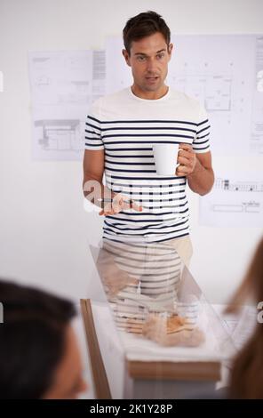 Dieses neue Projekt muss perfekt durchgeführt werden. Ein junger Mann, der seinen designenden Mitarbeitern eine Präsentation gibt. Stockfoto