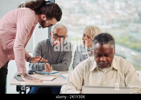 Eine multirassische Gruppe älterer Studenten spricht mit einem jungen Pädagogen über die Nutzung sozialer Medien im Klassenzimmer. Stockfoto