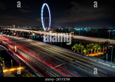 Singapore Flyer bei Nacht mit Autobeleuchtung auf der Autobahn im Vordergrund. Singapur Stockfoto