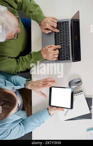 Der junge Pädagoge zeigt dem Studenten, wie er ein Problem auf seinem Tablet beim Projekt lösen kann, während der Schüler auf einem Laptop tippt. Stockfoto