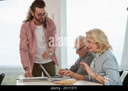 Ein junger Professor überprüft ältere Studenten, die Laptops in einem Klassenzimmer verwenden. Stockfoto