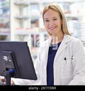 Lasst mich Eure Geschichte überprüfen. Porträt eines attraktiven Apothekers am Computer. Stockfoto