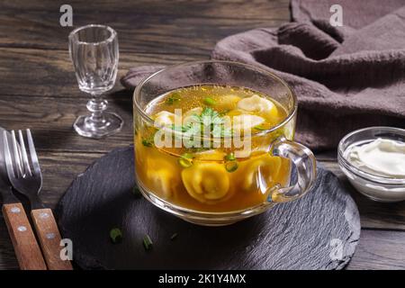 Frische Brühe mit Knödeln in Glasschüssel auf dem Tisch in der Nähe Stockfoto