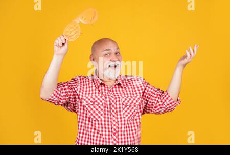 Staunender reifer Mann mit Partybrille auf gelbem Hintergrund Stockfoto