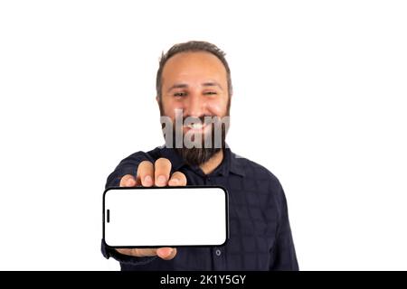 Halten Smartphone, glücklich lächelnd kaukasischen Mann hält Smartphone. Zeigt moderne horizontale Handy-Modell. Porträt eines bärtigen Mannes im Stehen. Stockfoto