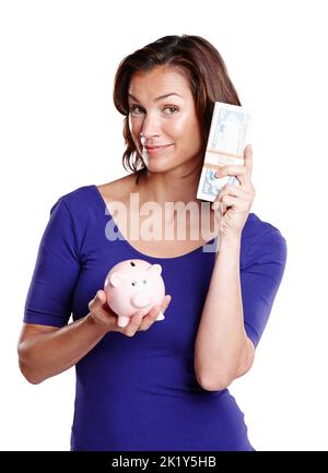 Sparen Sie Dollar und Cent. Studioporträt einer Frau Mitte 30s, die lächelt, während sie ein Sparschwein und einen Stapel Papiergeld hält. Stockfoto