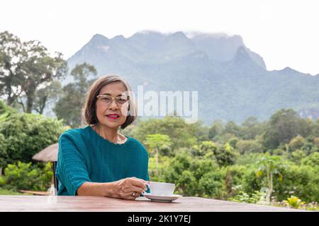 ASIN Senior Frau trinkt Kaffee im Cafe im Freien mit Blick auf die Berge. Stockfoto