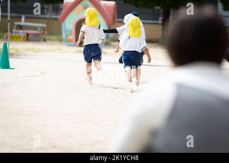 Kinder, die während eines Sporttages in einer japanischen Kindergarten-Vorschule auf dem Boden laufen Stockfoto