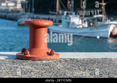 Ein rot orangefarbener Ankerplatz mit einem Fischerboot im Hintergrund Stockfoto