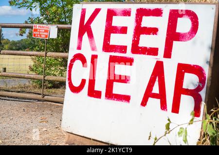 Großes, klares Schild an einem eingezäunten Eingang und kein Parkschild am Tor. Der Fokus liegt dabei auf dem NO-PARKING-Schild am Tor. Stockfoto