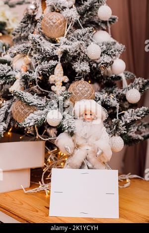 Grußkarte und Puppe stehen in der Nähe des Weihnachtsbaums Stockfoto