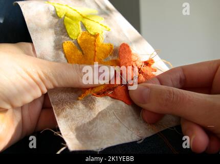 Nahaufnahme der Hände einer Frau, die näht, um appliqué-Arbeiten von Herbstblättern zu produzieren. Stockfoto