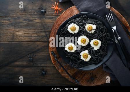 Halloween Party italienische schwarze Pasta dekoriert Horror Oliven wie Augen auf schwarzem Teller auf alten dunklen Tisch Hintergrund. Monster Gesicht von Pasta. Halloween Stockfoto
