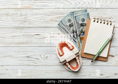 Flache Lay-Komposition mit pädagogischem Dentypodont Modell und Geld mit Notizbuch auf farbigem Tisch, Draufsicht. Teure Behandlung. Stockfoto