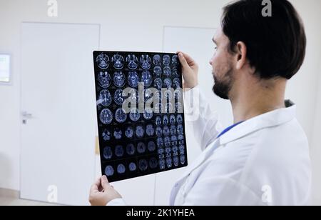 Allgemeinmediziner, der sich die MRT des menschlichen Gehirns ansieht und Anatomie und Pathologie des Gehirns des Patienten untersucht, während er im Korridorkrankenhaus steht Stockfoto