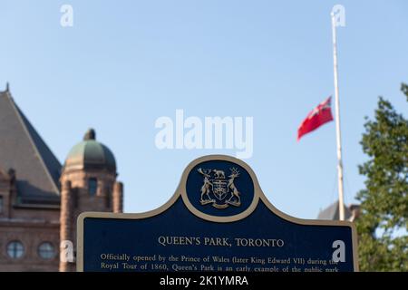 Ein Schild mit der Aufschrift Queens Park, der Heimat der Legislativversammlung von Ontario; gesehen mit der Flagge von Ontario bei der Hälfte des Personals nach dem Tod Königin Elizabeth II. Stockfoto
