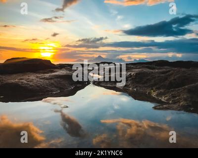 Sonnenuntergang farbenfroher Himmel, der sich im Meerwasser widerspiegelt. Helle Farben gegen Bergfelsen. Natürliche Sommerszene. Atemberaubender natürlicher Hintergrund. Panoramabild der Berge bei Sonnenuntergang. Reisen, Tourismus, Abenteuer Stockfoto