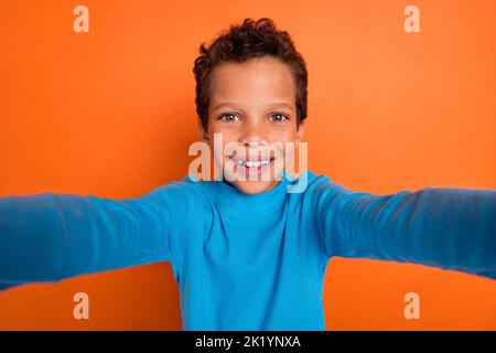 Foto-Porträt von entzückenden kleinen Jungen nehmen Selfie-Videoanruf Frontkamera gekleidet stilvolle blaue Kleidungsstück auf orangefarbenem Hintergrund isoliert Stockfoto