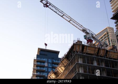 Eine Nahaufnahme einer Krankonstruktion bei der Arbeit an einem klaren Tag. In Betrieb, heben eines Stücks für eine Baustelle Baustelle, Bau einer Wohnung. Stockfoto