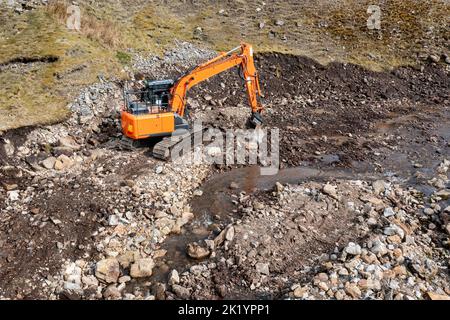 Orange Hydraulikbagger tun Bodenarbeiten Clearing Felsen und Steine erhöhte Ansicht Stockfoto