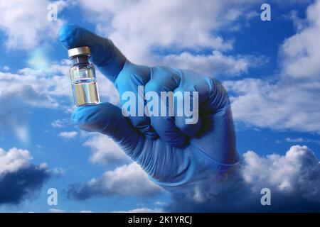 Eine Hand in einem blauen medizinischen Handschuh ragt aus den Wolken und hält eine Ampulle mit Impfstoff. Collage... Stockfoto