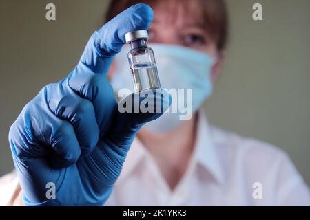Eine Ärztin hält ein Fläschchen mit Impfstoff in ihren Händen. Unscharfer Hintergrund... Stockfoto