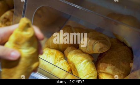 Nahaufnahme der Hände einer Frau, die in einer Bäckerei frisch gebackene Croissants nahm. Stockfoto