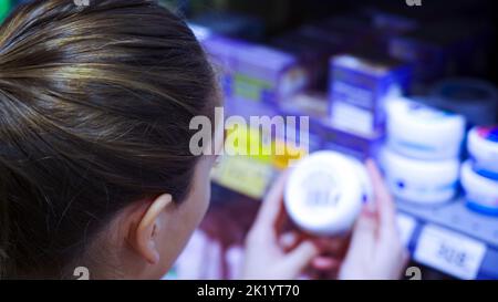 Eine junge Frau wählt in einem Supermarkt eine Kosmetikcreme Stockfoto