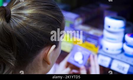 Eine junge Frau wählt in einem Supermarkt eine Kosmetikcreme Stockfoto