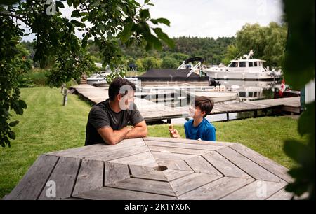 Mann und Junge essen Eiszapfen am Picknicktisch am sonnigen Tag. Stockfoto
