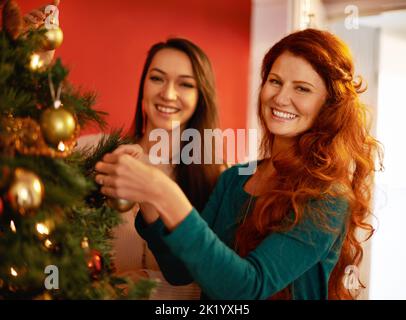Zwei attraktive junge Frauen dekorieren einen weihnachtsbaum. Stockfoto
