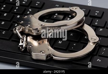 Computertastatur und Handschellen. Konzept für Cyberkriminalität, Internetsicherheit und Kriminalität. Stockfoto