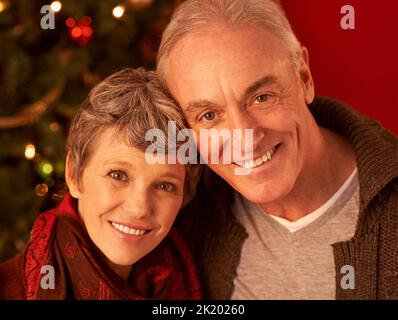 Es ist die schönste Zeit des Jahres. Ein zugeschnittenes Porträt eines glücklichen reifen Paares vor einem Weihnachtsbaum. Stockfoto