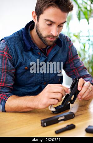 Regelmäßige Wartung ist für jeden Waffenbesitzer unerlässlich. Ein junger Mann, der seine Waffe putzt. Stockfoto