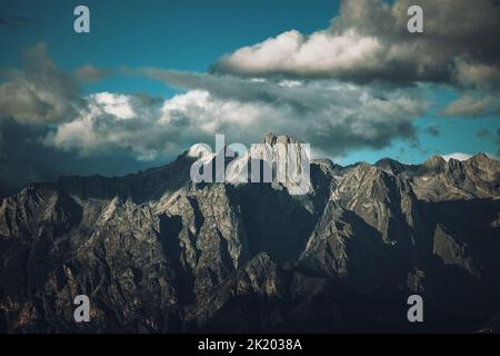Ein dunkler Berg aus der Ferne mit Sonnenstrahlen, die an einem halbbewölkten Tag auf den Gipfel treffen.gut für einen Desktop-Hintergrund. Stockfoto