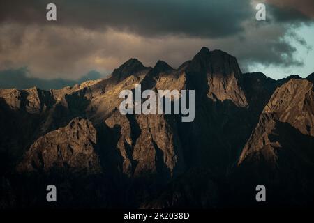 Ein dunkler Berg mit Sonnenstrahlen, die auf den Gipfel treffen, und Wolken am oberen Gipfel.Ideal für einen Desktop-Hintergrund. Stockfoto