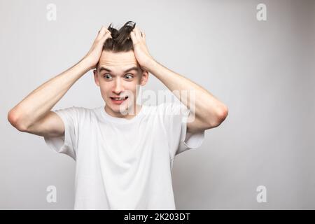 Porträt eines ängstlich jungen Mannes, der seine Hände in Panik am Kopf hält. Studio auf grauem Hintergrund aufgenommen Stockfoto