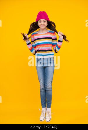 Ein erstaunlicher Teenager. Springt und lauft. Schöne Winter Kinder Porträt. Teenager Mädchen posiert mit Winter Pullover und Strickmütze auf gelbem Hintergrund. Aufgeregt Stockfoto