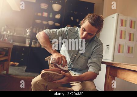 Ein hübscher junger Mann, der seine Schuhe in der Küche putzt. Stockfoto