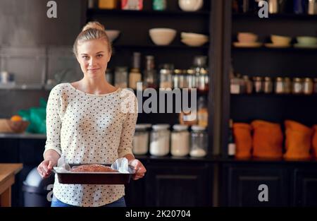 Nichts ist besser als hausgemachtes Brot. Porträt einer jungen Frau, die einen frisch gebackenen Brotlaib in einer Pfanne hält. Stockfoto