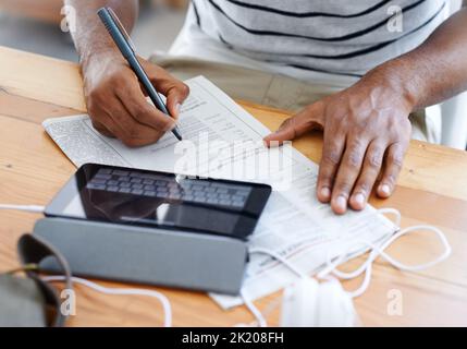 Notizen machen, während er arbeitet. Beschnittene Ansicht eines afroamerikanischen Mannes, der an seinem Schreibtisch an einem digitalen Tablet arbeitet. Stockfoto