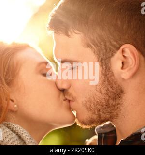 Jeder Kuss fühlt sich an wie unser erster. Ein glückliches junges Paar, das einen Kuss im Freien teilt. Stockfoto