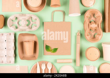 Flache Komposition im Lay-Stil mit Öko-Geschirr-Bundle, Papierutensilien, Papiertüte und -Halter, Holzbesteck auf hellgrünem Hintergrund. Sust Stockfoto