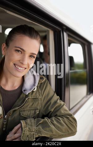 Genießen Sie die Fahrt. Eine attraktive junge Frau, die durch das Autofenster schaut, während sie auf einer Autofahrt unterwegs ist. Stockfoto