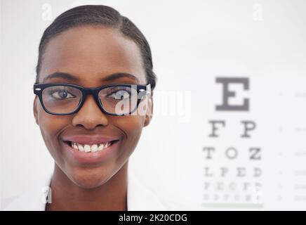 Ich kann jetzt klar sehen. Porträt einer weiblichen Optometristin, die neben einer Augentestkarte steht. Stockfoto