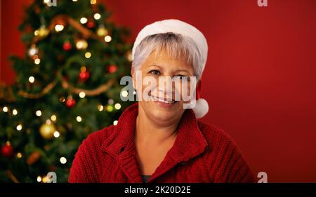 Fröhliches Gefühl. Beschnittene Studioaufnahme einer reifen Frau, die in ihrem weihnachtshut glücklich aussieht. Stockfoto