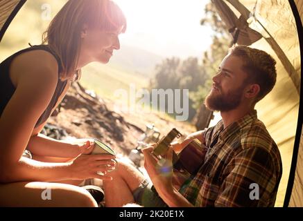 In den Wald. Ein junger Mann, der mit seiner Freundin in einem Zelt Gitarre spielt. Stockfoto