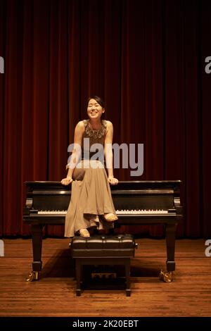 Shes eine professionelle Klavierspielerin. Eine junge Frau sitzt am Ende eines musikalischen Konzerts auf ihrem Klavier. Stockfoto