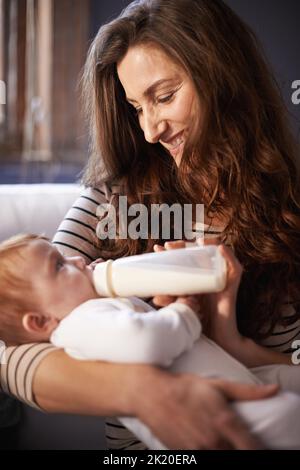 Eine anbetende Mutter, die ihrem Baby eine Flasche schenkt. Stockfoto