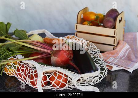 Gemüse in Öko-Einkaufstasche Mehrweg-Beutel und Holzkiste Tomaten, lila Kartoffeln, Auberginen, Karotten, Paprika, Rote Bete. Ökologisches Anliegen, Öko Stockfoto